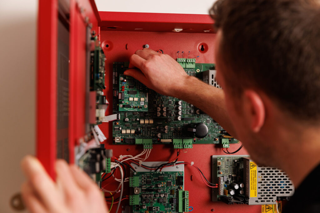 A member of the Advanced Technical Support team working on the inside of an addressable fire alarm system panel